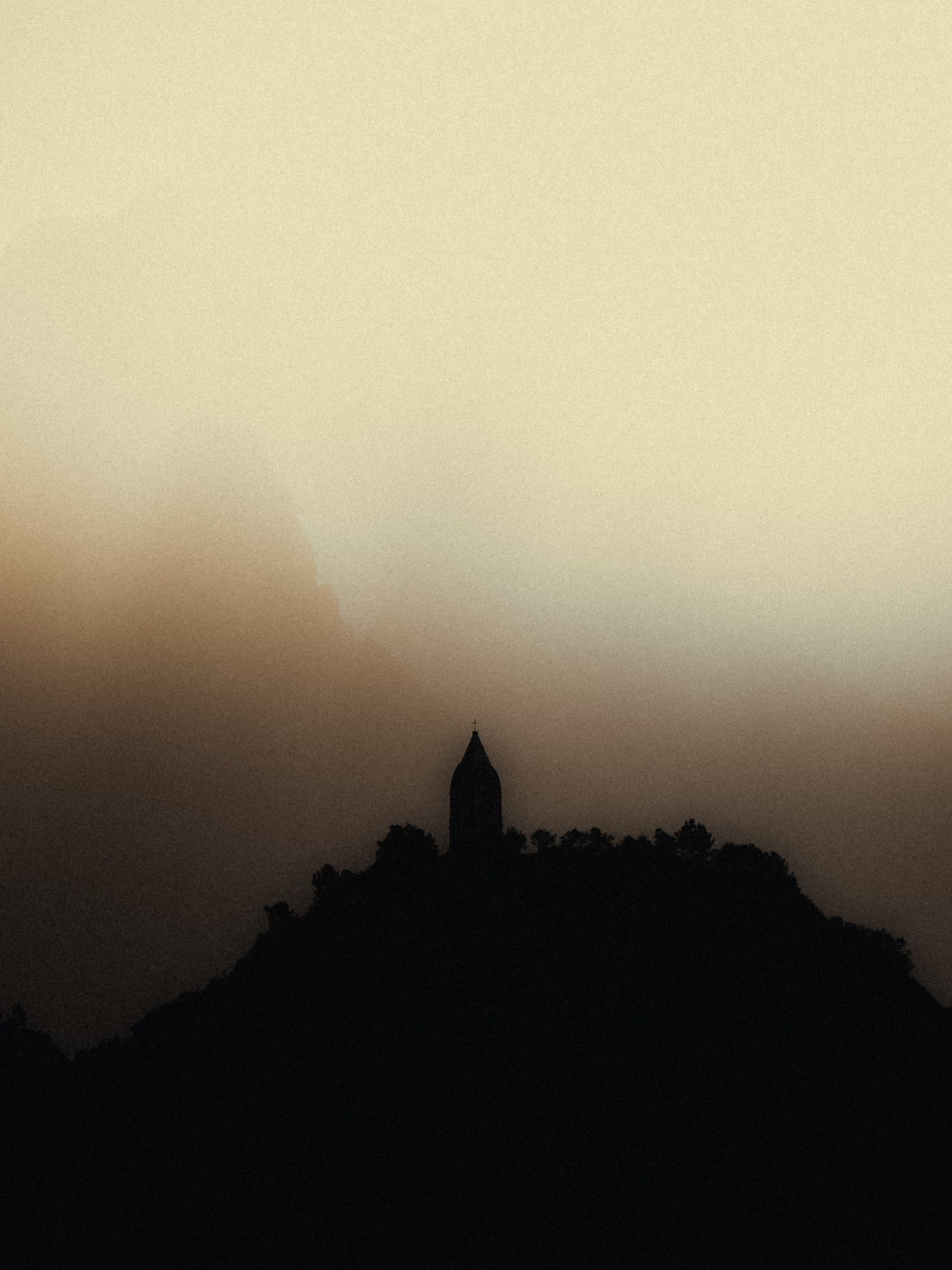 A distant chapel silhouetted on a Madeira ridge beneath a luminous wall of mist.