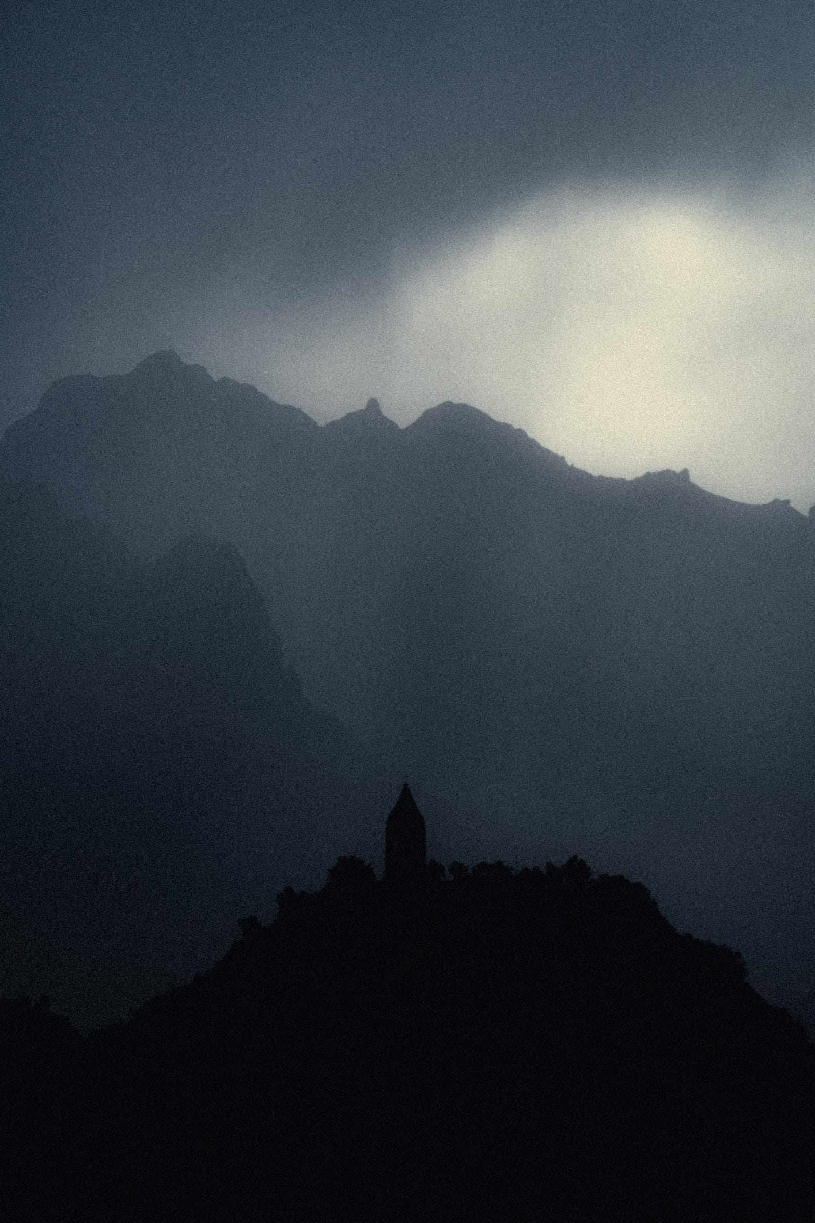 A small chapel silhouetted against layered Madeira peaks and a darkening sky.