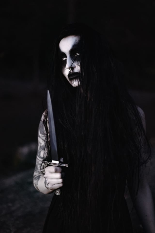 Ett black metal inspirerat porträtt av en långhårig gestalt med en dolk i djup skugga