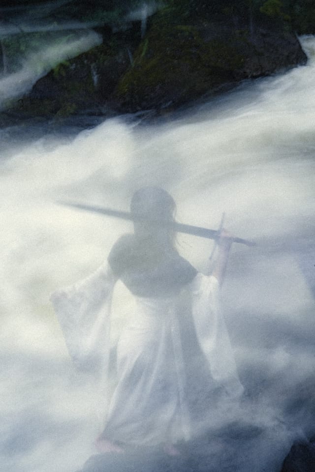 A spectral figure holding a sword across her body within a veil of rushing water