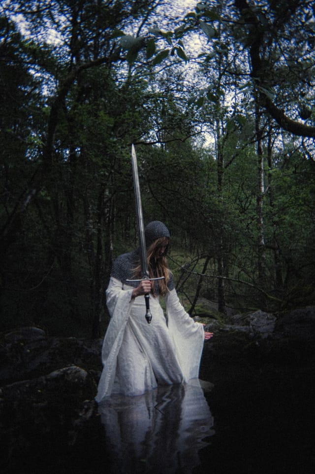 A solitary sword-bearer standing in a dark forest stream