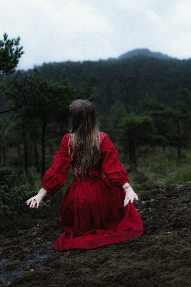 A woman in red opening her hands to a quiet Norwegian landscape