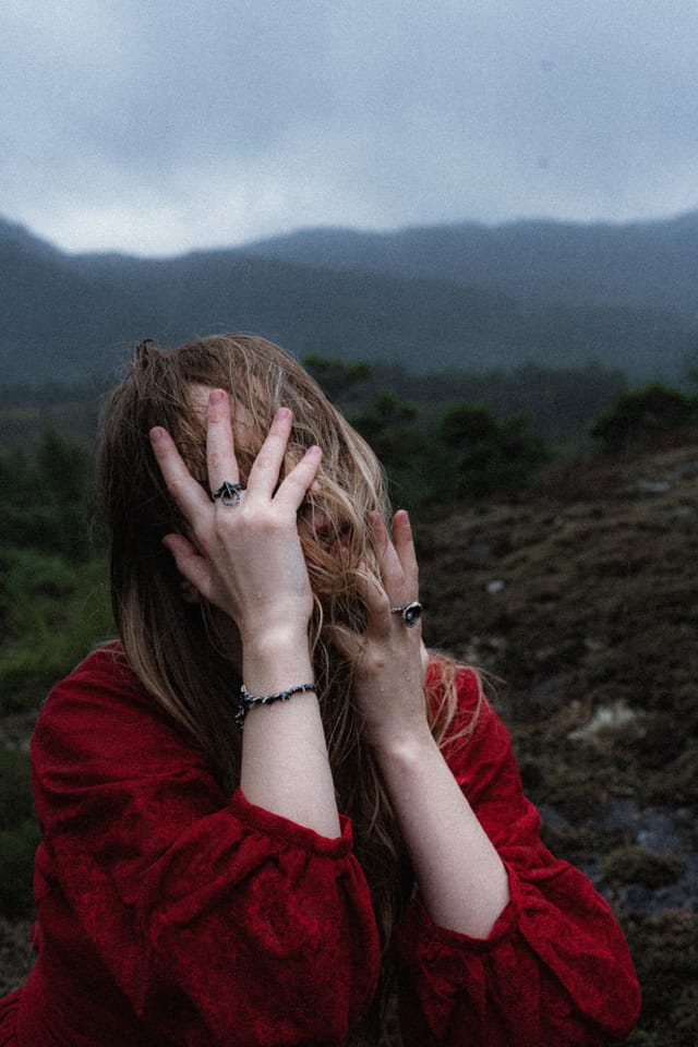 An intimate portrait of a red-clad woman veiling her face with both hands