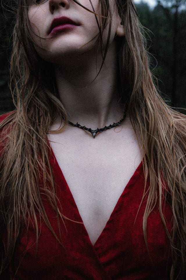 A close portrait of wet hair, dark lipstick and silver jewellery above red fabric