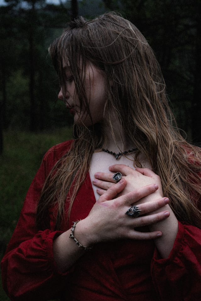 A rain-soaked woman in red holding both hands over her chest