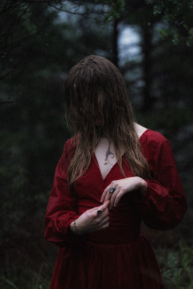 A wet-haired woman in red looking down while gathering her jewellery