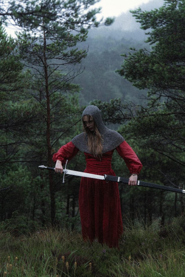 A red-clad sword-bearer drawing the blade across her body among pines