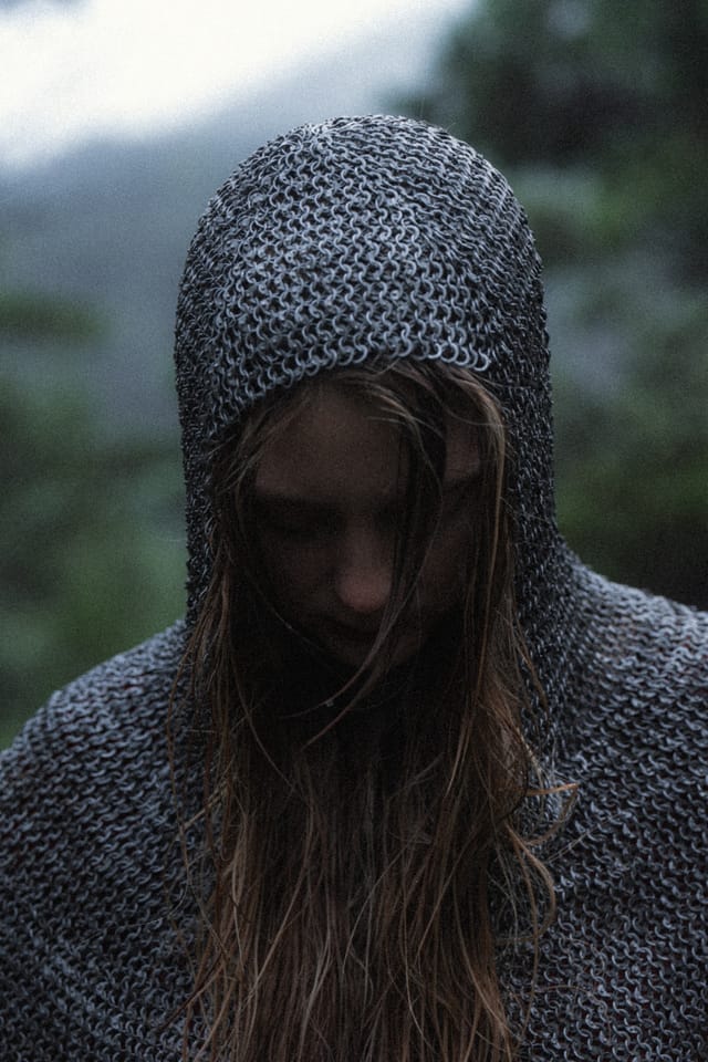 A distant woman in red holding a sword upright in a misty clearing