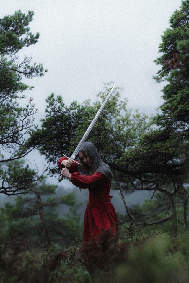 A solitary sword-bearer in red standing beneath pale mountain fog