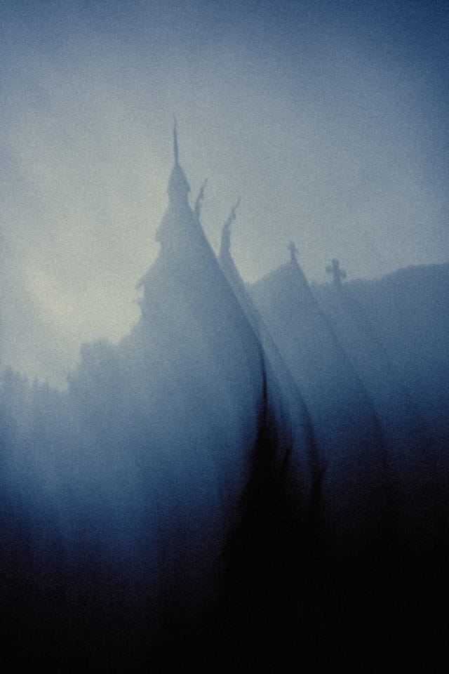 A motion-softened stave church spire emerging through blue mountain mist