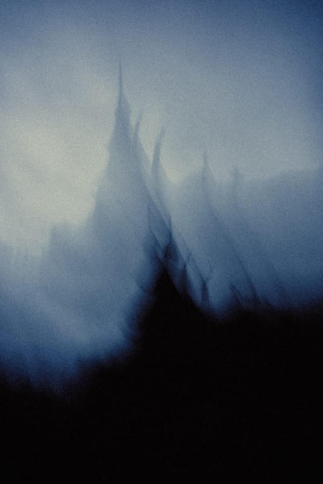 A blurred stave church roof rising like a dark flame against pale fog