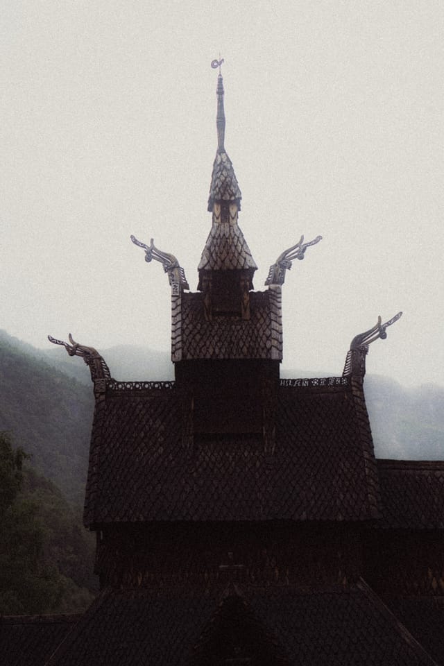 A full stave church facade beneath pale grainy mountain light