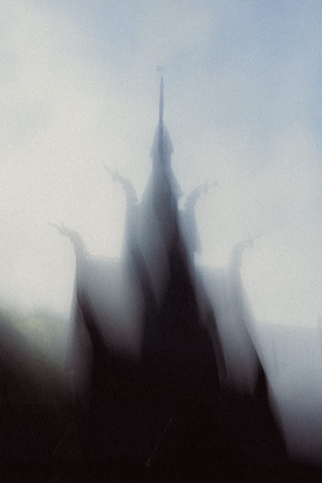 A blurred stave church spire rising from a dark roof against luminous haze
