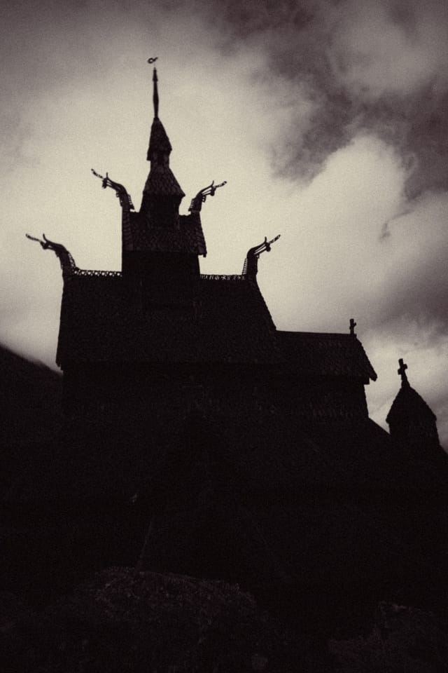 A stave church tower and dragon-head rooflines silhouetted beneath churning clouds