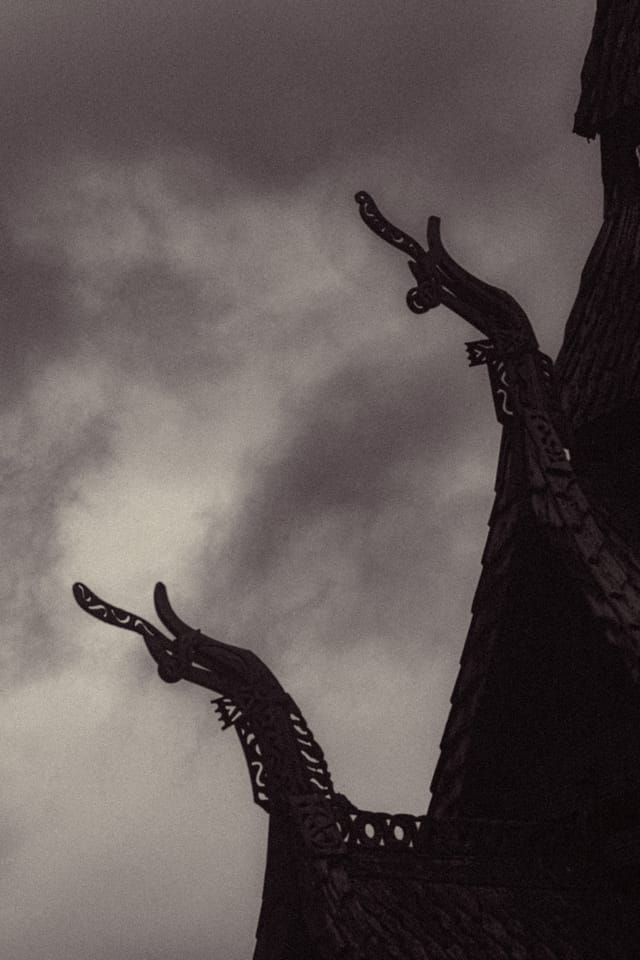 Close silhouettes of carved dragon-head roof finials against mottled cloud