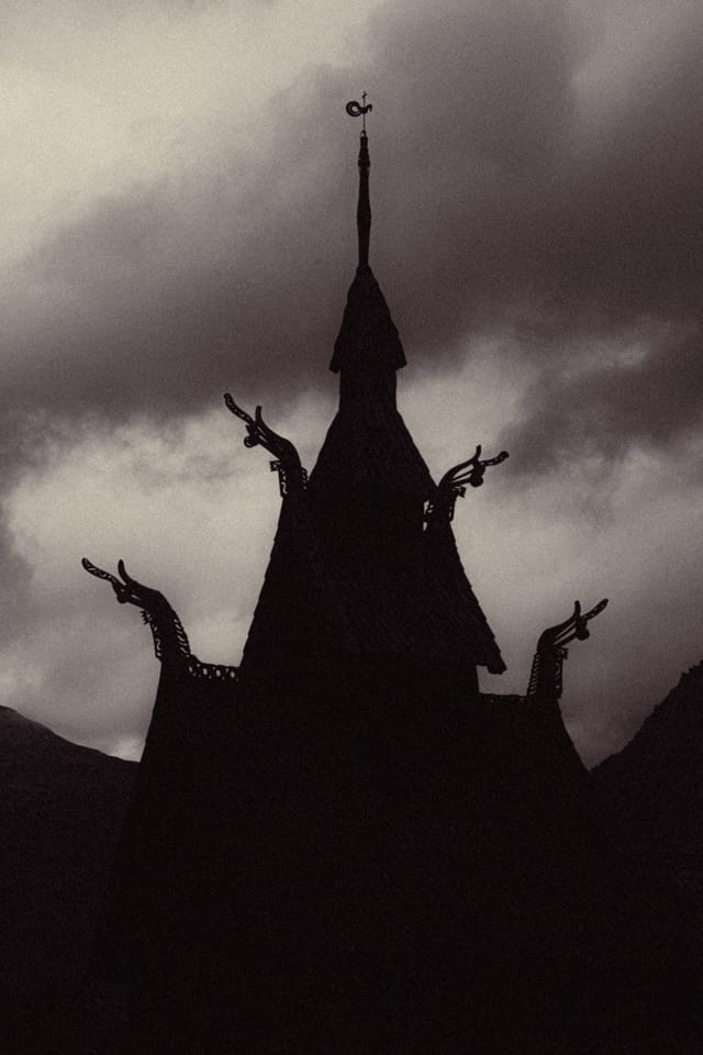 A stave church spire and dragon-head gables silhouetted beneath heavy clouds