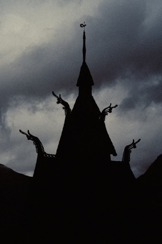 The dark roofline of a stave church set against a blue-grey cloud bank