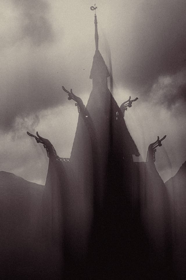 A monumental stave church spire framed by carved gables and restless clouds