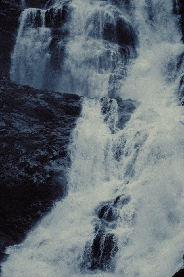 A broad waterfall dividing around black rock ledges