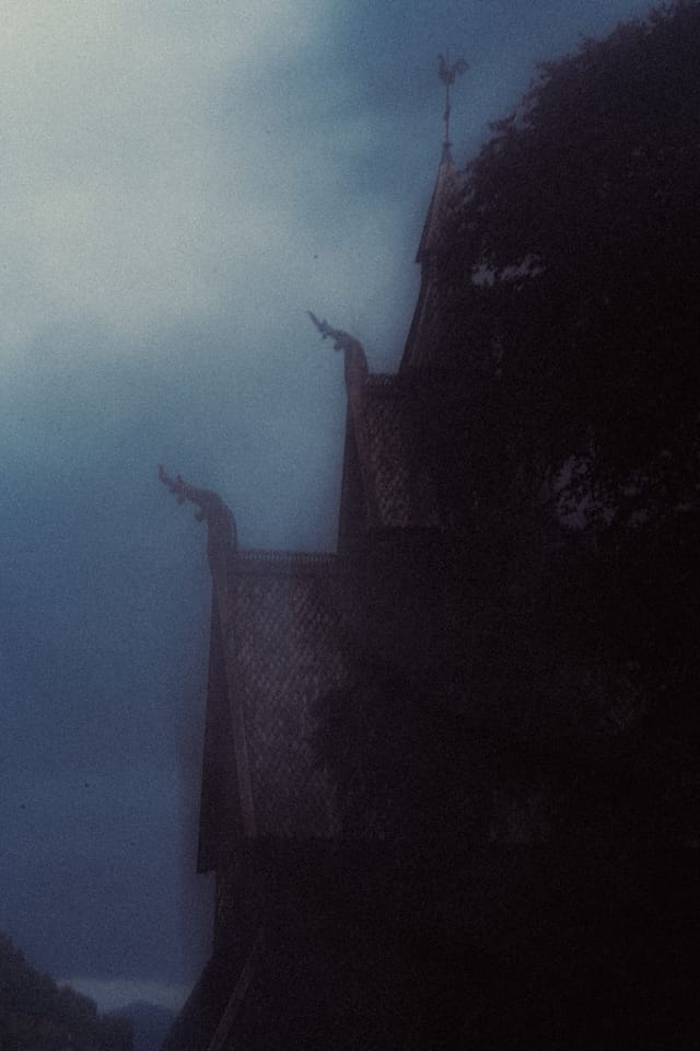 A blue-toned stave church roofline dissolving into fog