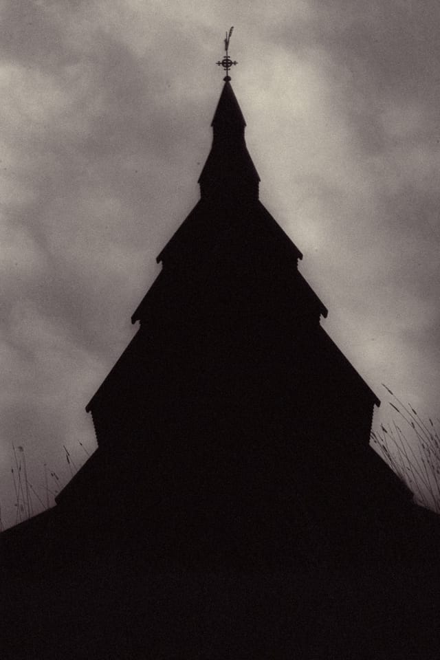 A stave church tower rendered as a stark silhouette beneath grainy clouds