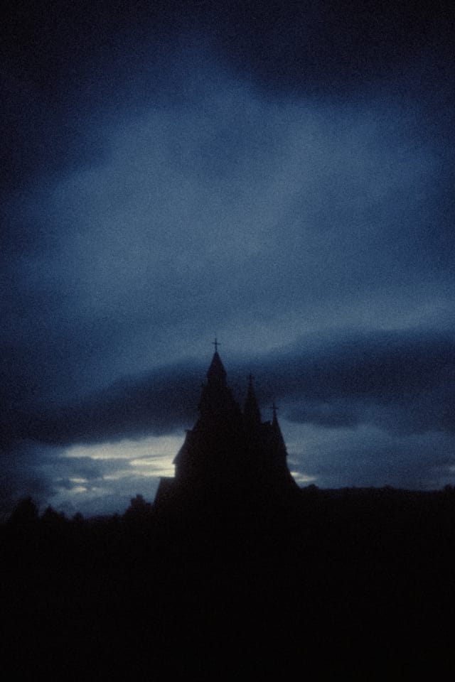 A distant stave church silhouette beneath a deep blue break in storm clouds
