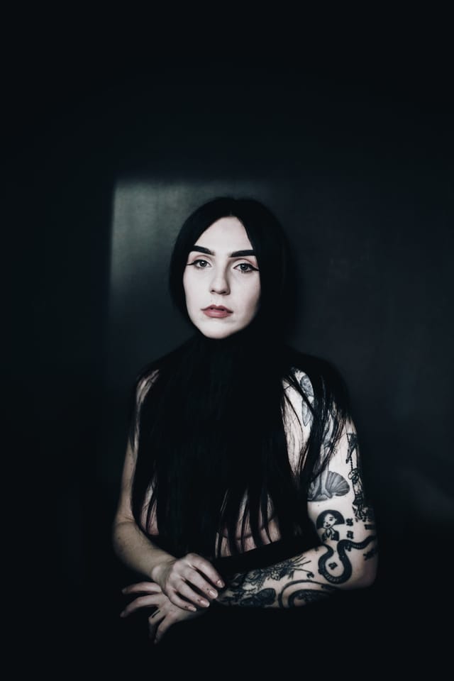 Cheri seated in a dark interior, framed by window light and deep shadow