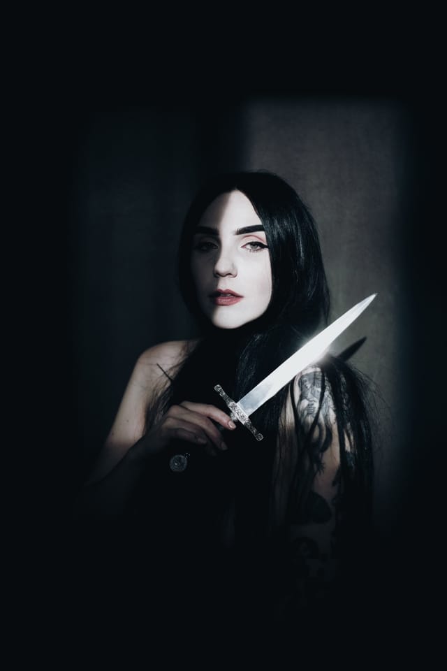 A bright dagger crossing the foreground of a shadowed portrait of Cheri